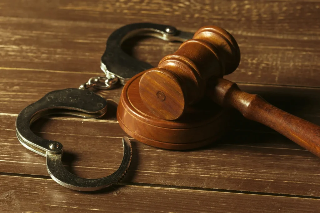 Shown are handcuffs and a judge's gavel on a table in the context of criminal law.